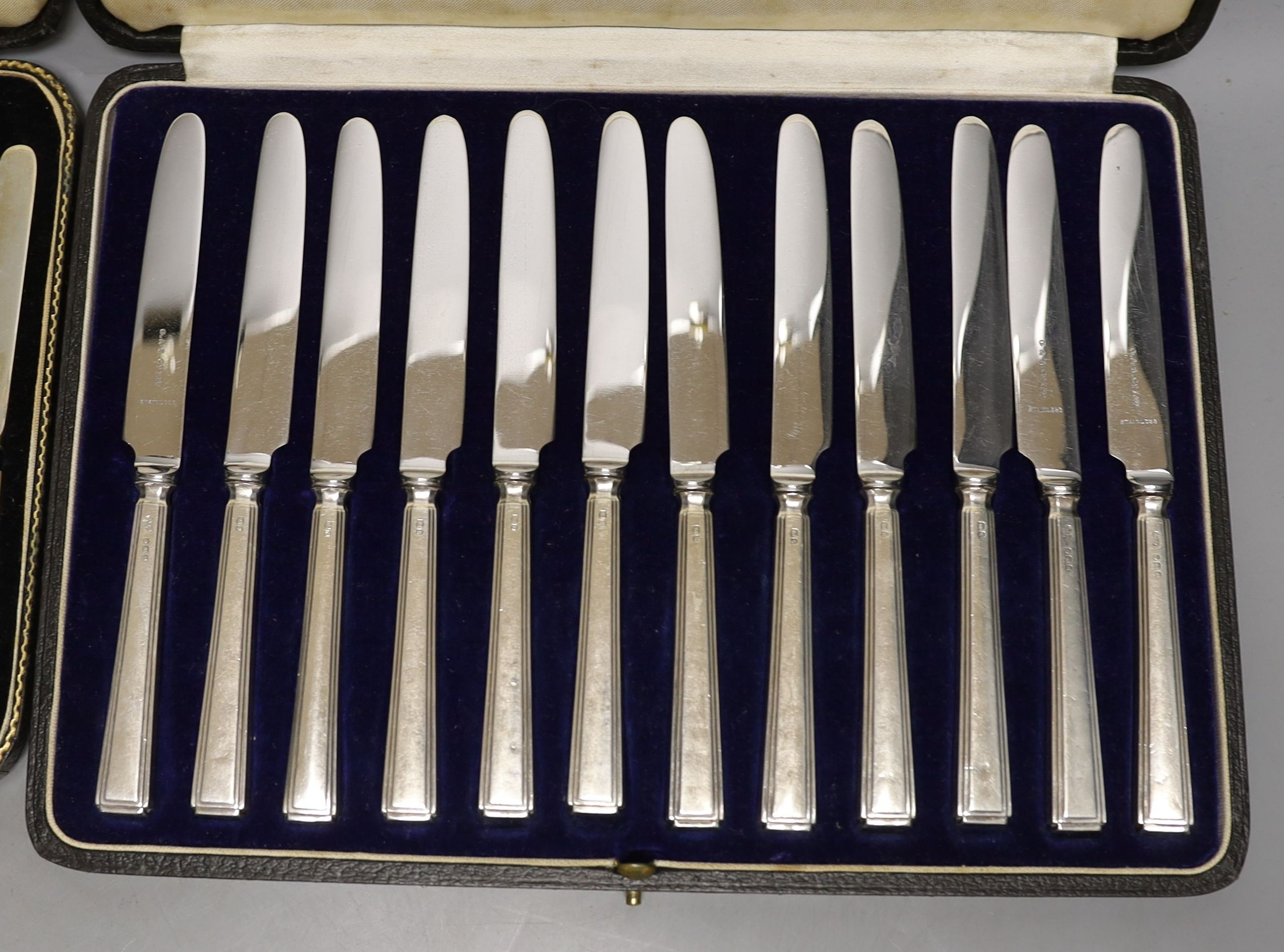 Two cased sets of silver or mother of pearl handled tea knives and a cased set of six silver teaspoons.